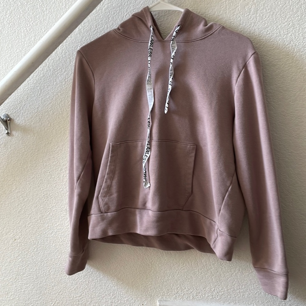 Pinkish-brown hoodie with pockets that says “flawless” on draw straps.